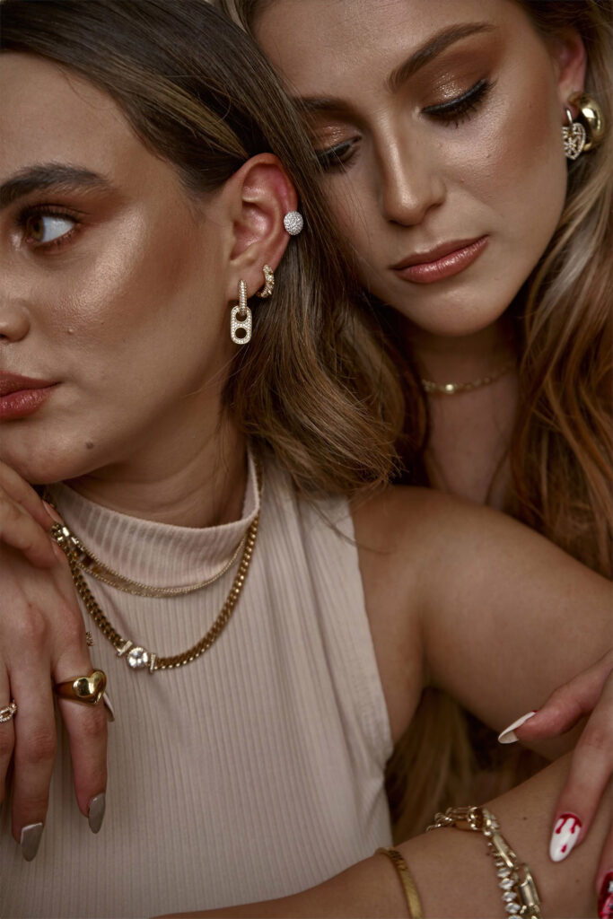 Clarisa and Valeria two women with striking features are captured in a close-up shot. They wear intricate jewelry including earrings necklaces and rings. Their makeup is meticulously done with emphasis on their eyes and lips. The image exudes a sense of elegance and sophistication.